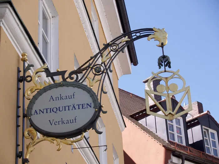 Ein schmiedeeisernes Ladenschild ragt von einer Hauswand in die Straße